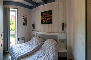 A bedroom with two beds, a window with curtains, a radiator, and a painting on the wall.