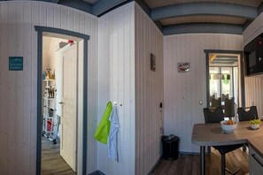 A room with a wooden floor, a dining table with chairs, a kitchen area with a stove, and a door leading to another room.