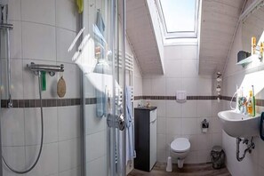 A modern bathroom with a glass shower enclosure, a toilet, and a sink with toiletries.