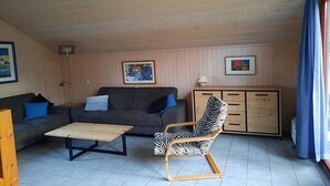 Ett vardagsrum med en soffa, en stol med zebrasträck, ett träskåp och två inramade tavlor på väggen.