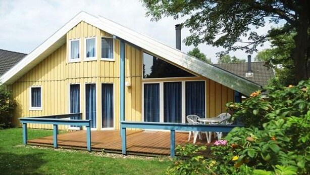 A yellow wooden house with a sloped roof, a wooden deck, and a small patio area with a table and chairs. - exklusives skandinavisches Ferienhaus (Granzow)