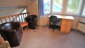 A room with a wooden ceiling, a desk with a chair, a black leather chair, a wooden dresser, and a window with a view of a blue house. - exklusives skandinavisches Ferienhaus (Granzow)