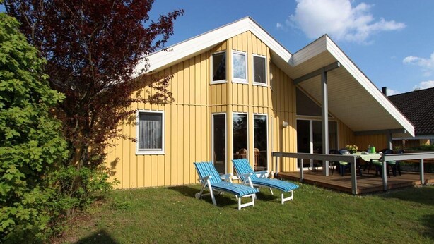 A yellow building with a deck, two lounge chairs, and a table with chairs. - skandinavisches Ferienhaus in Mirow (Granzow)