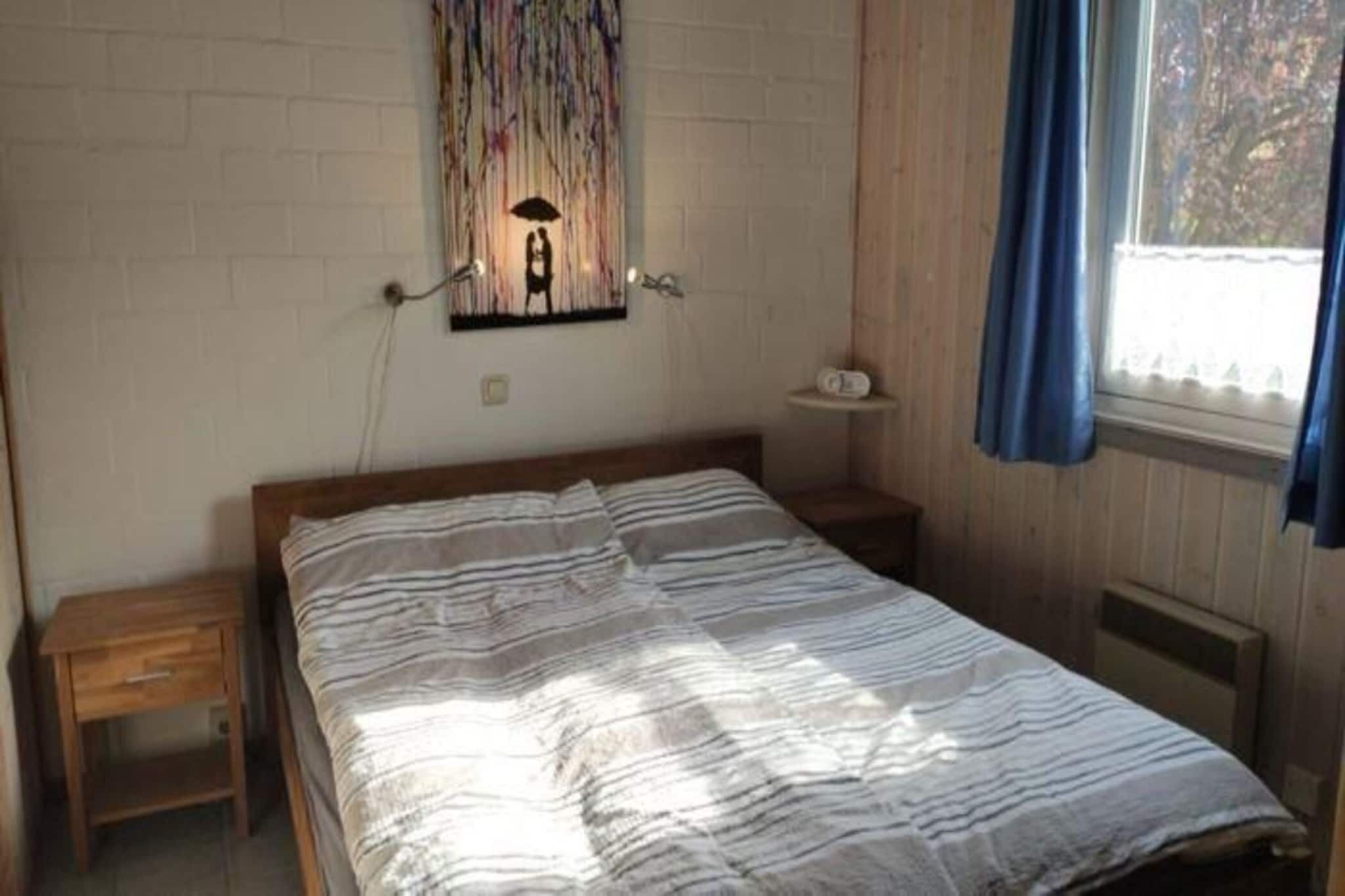 Een slaapkamer met een bed, nachtkastje, een wandlamp en een raam met gordijnen.