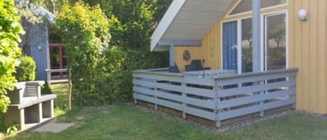 A covered outdoor deck with a white railing, a concrete bench, and a small table.