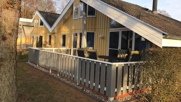 Ein zweistöckiges Haus mit einem geneigten Dach, einer überdachten Veranda mit Sitzgelegenheiten und einem Schornstein.