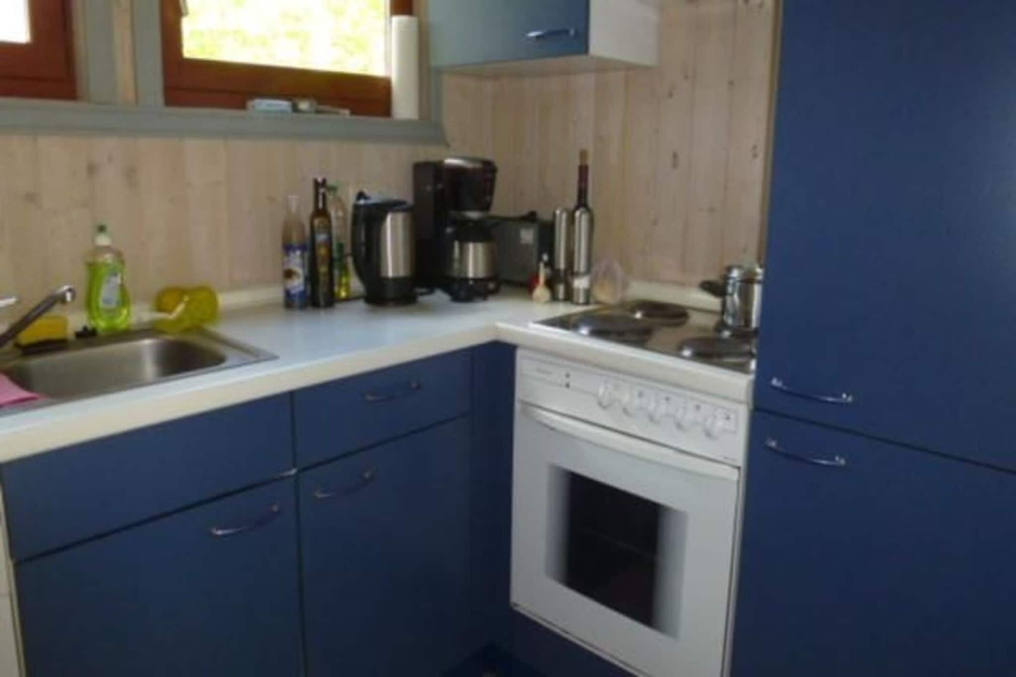 Una cucina con mobili azzurri, un piano cottura bianco e diversi elettrodomestici, tra cui una macchina da caffè e un bollitore.