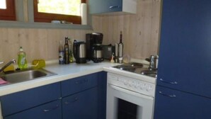 A kitchen with blue cabinets, a white stove, and various appliances including a coffee maker and a kettle. - Ferienhaus im Ferienpark Mirow (Granzow)