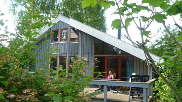 A two-story cabin with a balcony, surrounded by greenery. - Ferienhaus im Ferienpark Mirow (Granzow)