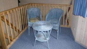 A balcony with two wicker chairs and a small round table, wooden railings, and a blue curtain. - Ferienhaus im Ferienpark Mirow (Granzow)
