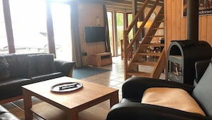 A cozy living room with a sofa, a coffee table, a fireplace, and a staircase leading to an upper level. - Ferienhaus im skandinavischen Stil (Granzow)