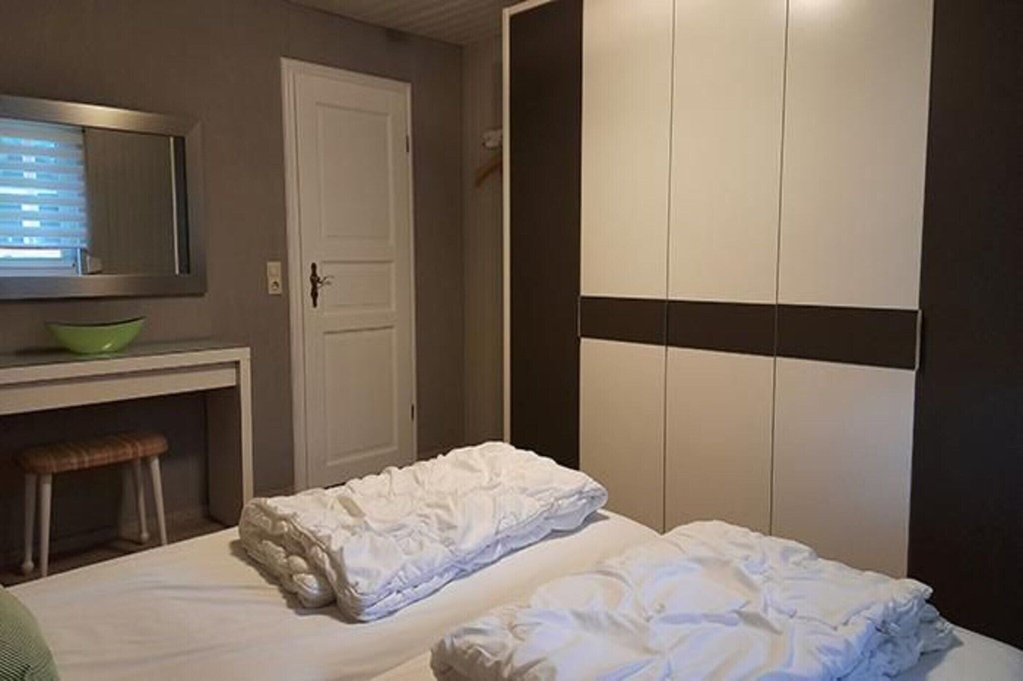 A hotel room with a bed, a bench, a mirror, and a wardrobe.