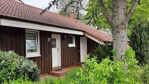 Una casa de un piso con fachada marrón, techo de tejas rojas y puerta blanca.