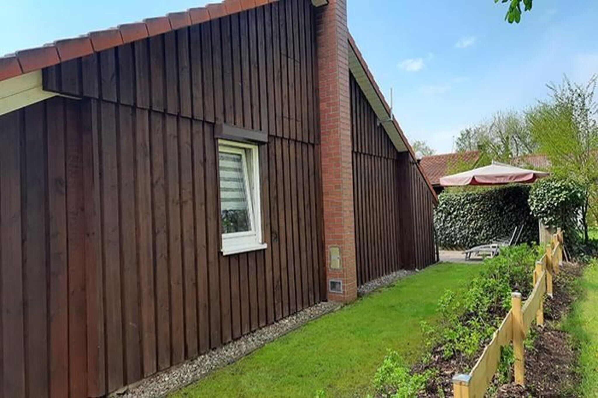 En træbygning med skorsten i mursten, et vindue og en have med træhegn og planter.
