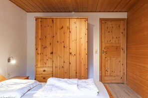 A bedroom with a wooden wardrobe, a bed with white bedding, and a wooden door.