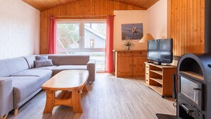 Un accogliente soggiorno con soffitto in legno, un divano, un tavolino in legno, una televisione e un camino.