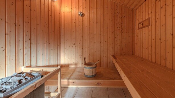 Una sauna con pareti e panche in legno, un catino e una panca con un vassoio di pietre.