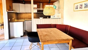 Een kleine keuken met witte kastjes, een houten tafel en een rode bank met kussens.