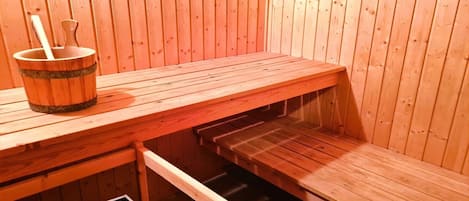 Un sauna avec des bancs en bois et un seau contenant une brosse.