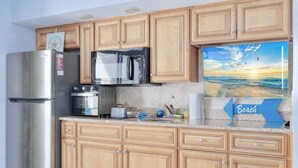 A kitchen with wooden cabinets, stainless steel appliances, and a beach-themed wall decoration.