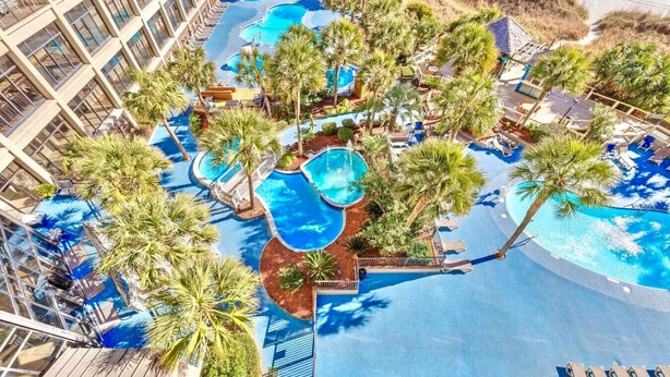 An aerial view of a resort with multiple swimming pools surrounded by palm trees and lounge chairs.