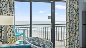 A room with a view of the beach, a sofa, a lamp, and a 'No Smoking' sign.