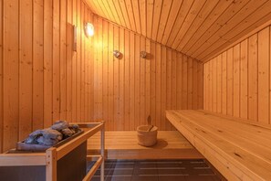 Una sala de sauna con paredes de madera, bancos, una pileta de piedra y luces empotradas.
