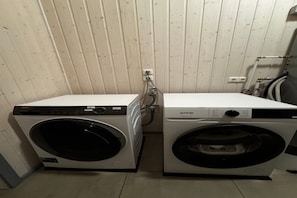 Two front-loading washing machines in a laundry room with a wooden wall and a visible plumbing fixture.