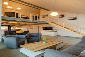 A spacious living area with a high ceiling, a wooden staircase, and a modern kitchen in the background.