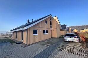 A modern two-story house with a sloped roof, a driveway, and a parked car.