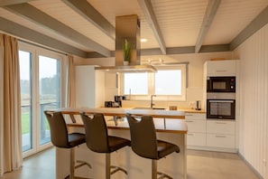 A modern kitchen with a central island, bar stools, a microwave, and a built-in oven.