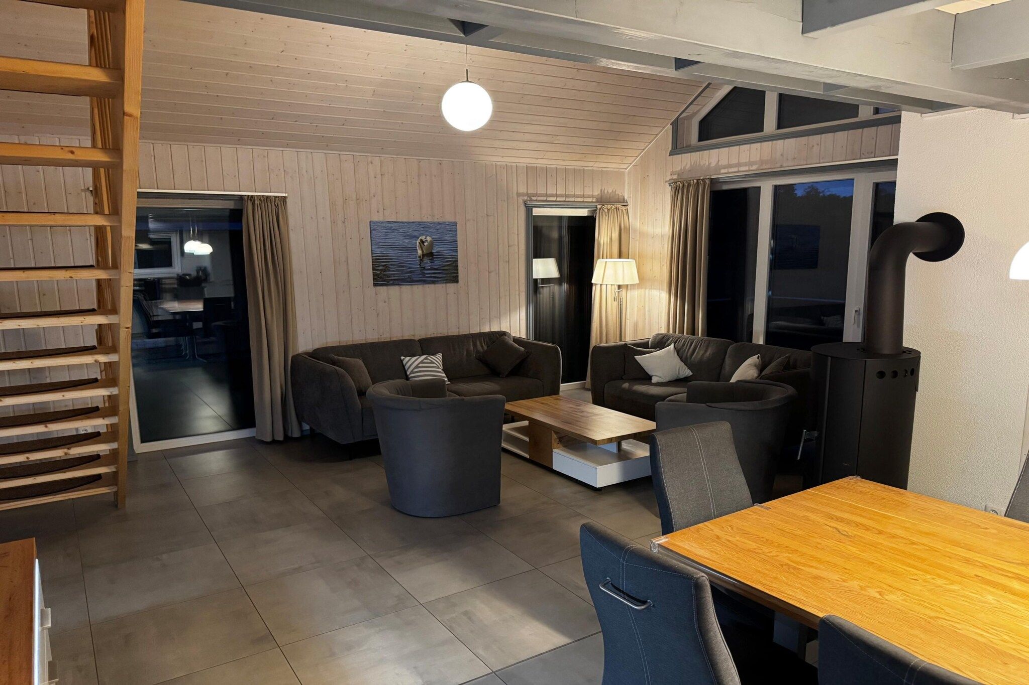 A modern living room with a sofa set, a coffee table, and a dining table. There is a fireplace and a view of the outdoors.