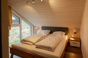 A bedroom with a bed, a nightstand, a lamp, and a window. - Ferienhaus im skandinavischen Stil (Granzow)