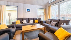 A modern living room with a sofa set, a coffee table, and large windows offering a view of the outdoors.