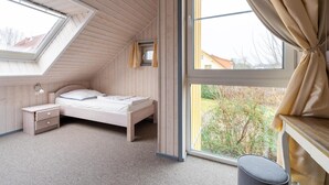 A bedroom with a sloped ceiling, a skylight, a bed, a nightstand, a small window, and a view of the outside.