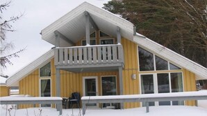 A two-story wooden building with a balcony, large windows, and a snow-covered ground.