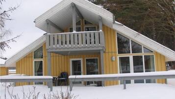 A two-story wooden building with a balcony, large windows, and a snow-covered ground.