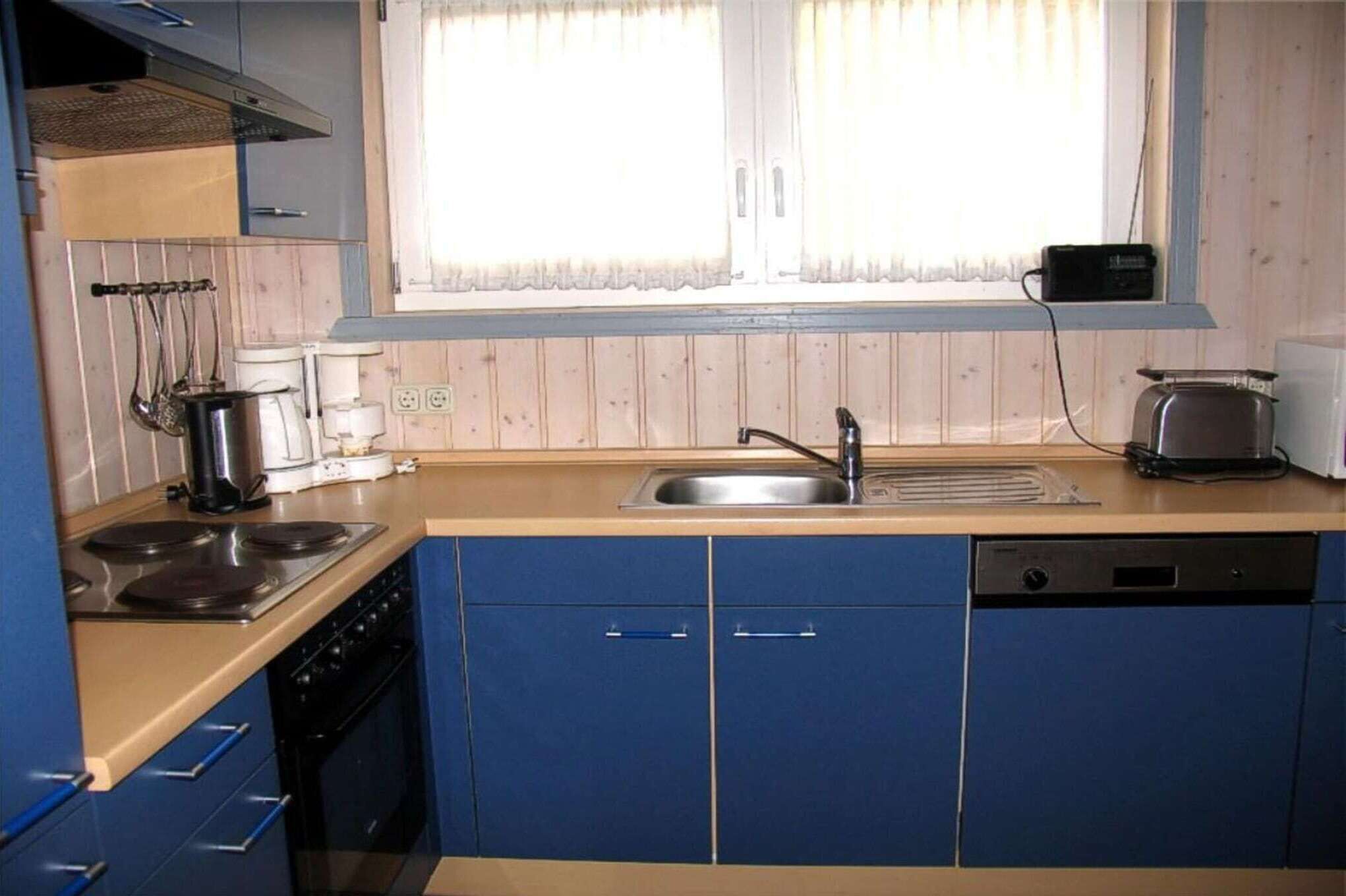 A kitchen with blue cabinets, a stove, a sink, and a window with curtains.