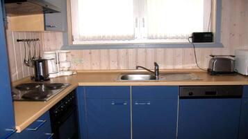 A kitchen with blue cabinets, a stove, a sink, and a window with curtains.