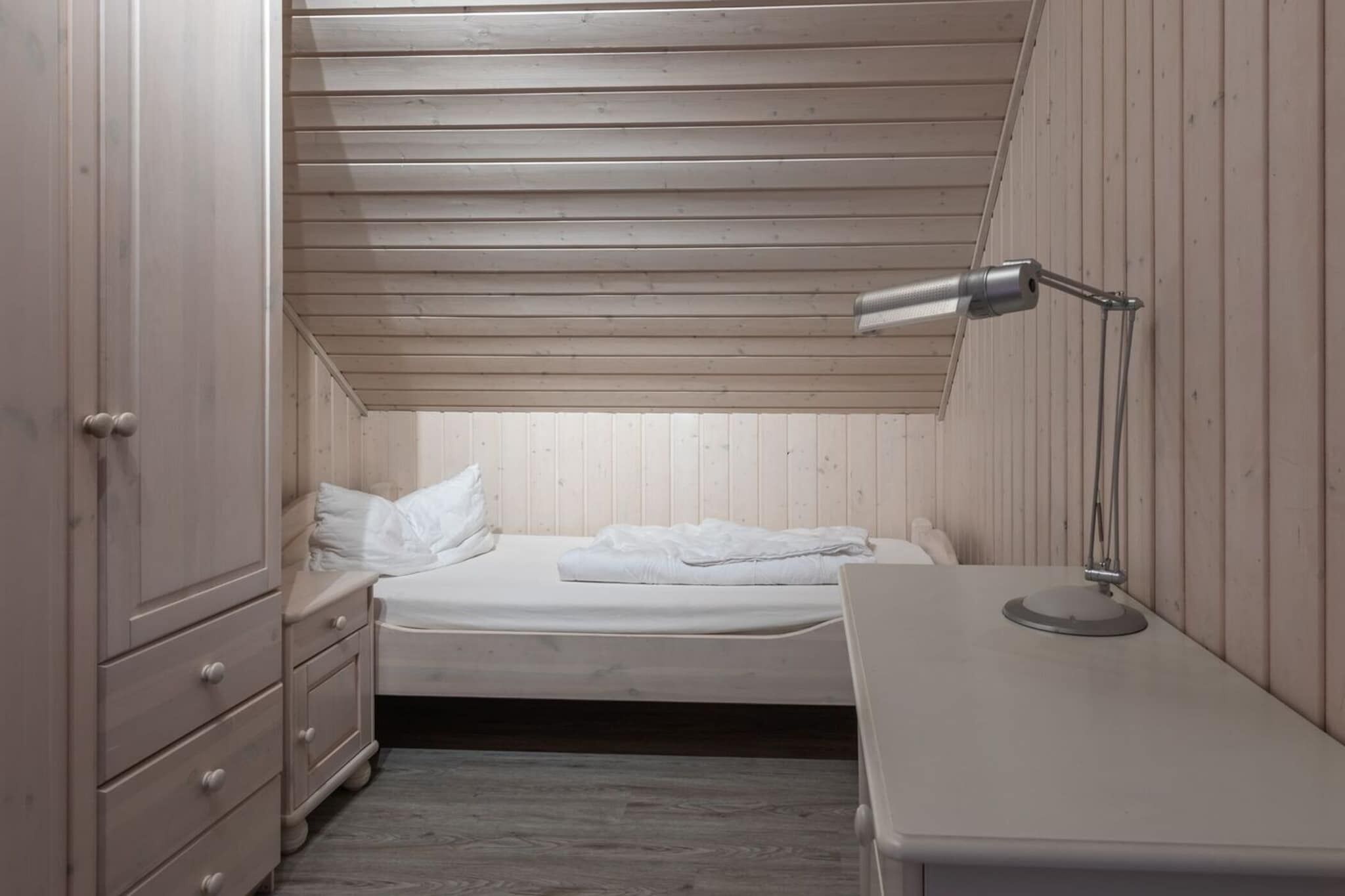 A small, single-bed room with a sloped ceiling, a bedside table, a lamp, and a wardrobe.
