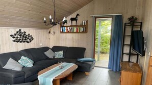 Ett mysigt vardagsrum med en hörnsoffa, ett soffbord i trä, en bokhylla och en tv som står på ett träställ.