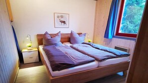 A wooden bed with two pillows and a blanket, a nightstand with a lamp, and a window with a curtain. - skandinavisches Ferienhaus in Mirow (Granzow)
