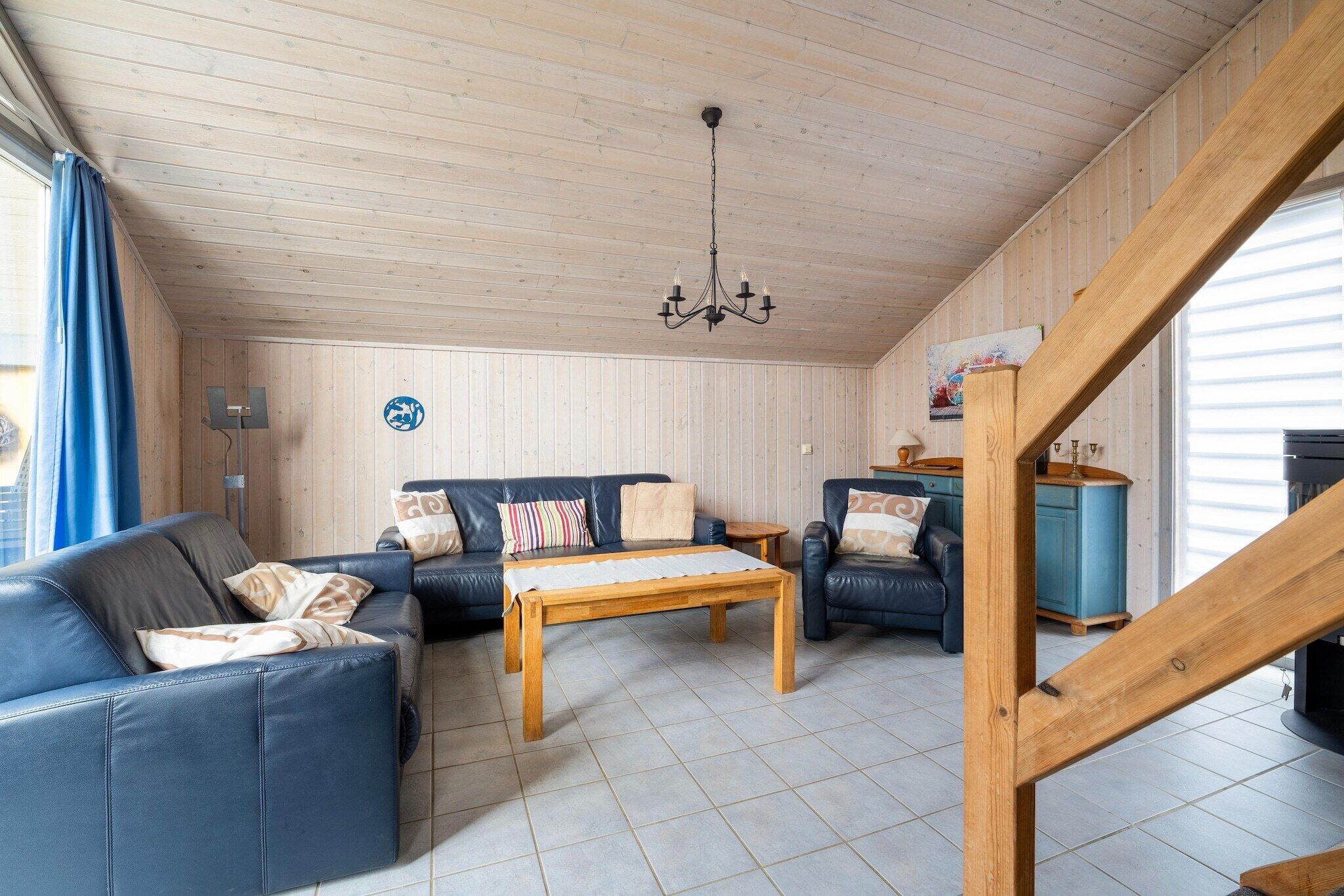 A cozy living room with a wooden ceiling, a chandelier, a sofa set, a coffee table, and a blue cabinet.
