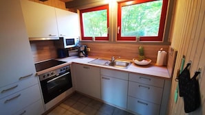 A compact kitchen with white cabinets, a stove, a sink, and two windows with red frames. - skandinavisches Ferienhaus in Mirow (Granzow)