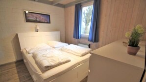 Ein Schlafzimmer mit Bett, Nachttisch, Topfpflanze, einem Fenster mit Vorhängen und einem Bild an der Wand.