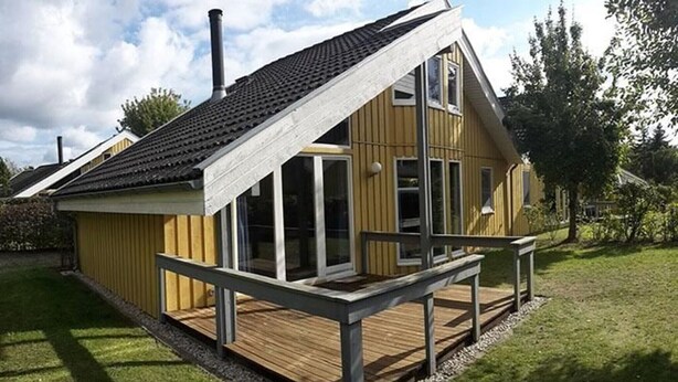 Ein modernes Haus mit geneigtem Dach, großen Fenstern und einer Holzterrasse.