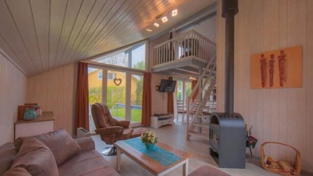 A cozy living room with a sofa, a coffee table, a fireplace, and a balcony with a wooden railing. - Ferienhaus im Ferienpark Mirow (Granzow)