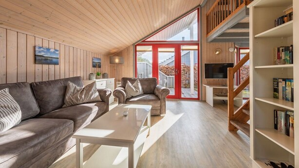 A modern living room with a wooden ceiling, a sofa set, a coffee table, and a bookshelf.