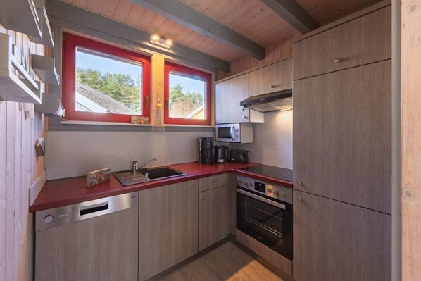 Une cuisine compacte avec des meubles en bois, un plan de travail rouge, un four encastré et une fenêtre dotée d’un cadre rouge.