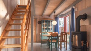 Ein Holzinnenraum mit einer Treppe, einem Essbereich mit Stühlen und Tisch, einer Schrank mit Glastüren und einem Herd.
